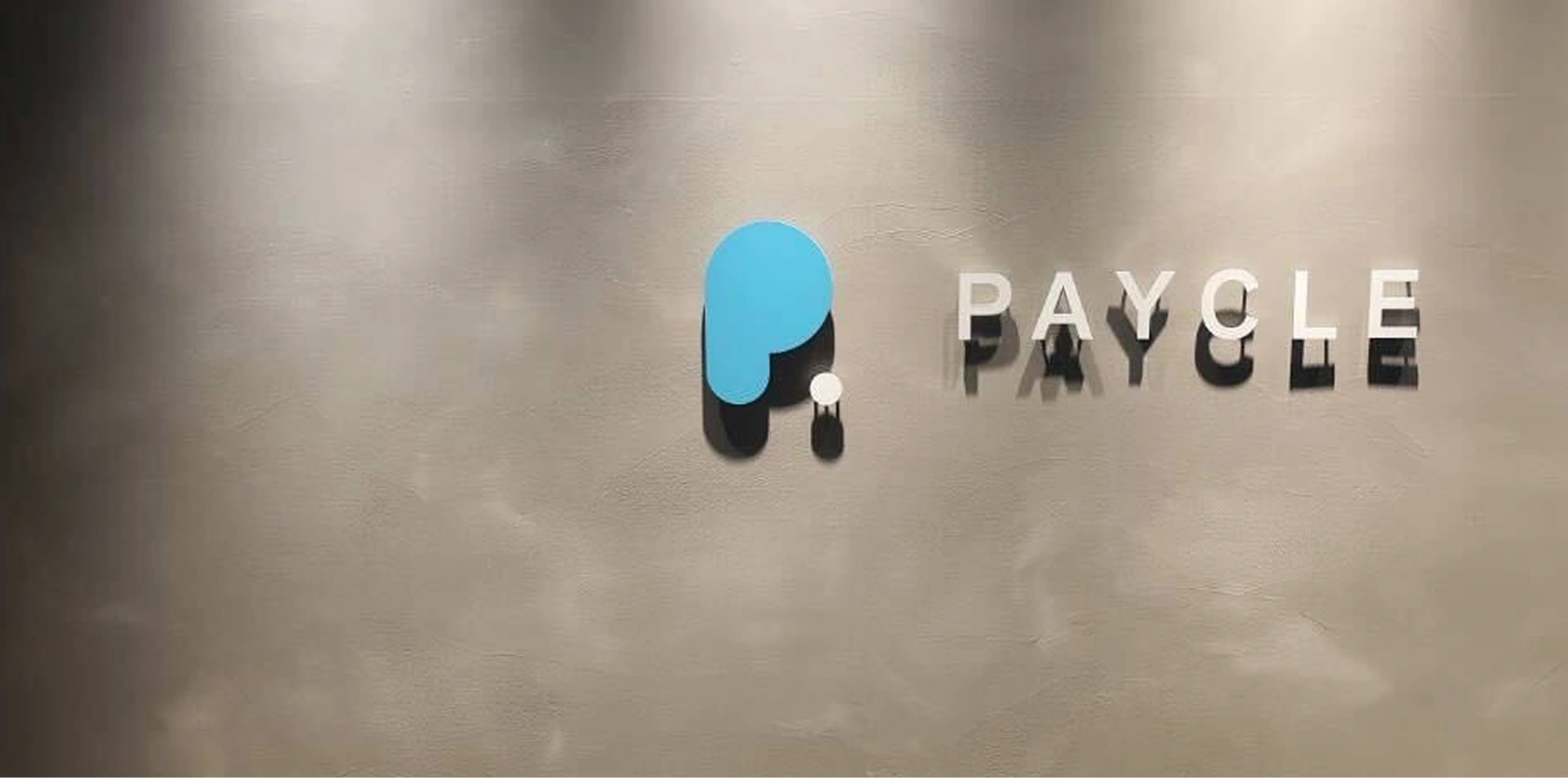 グレーの壁面に設置された、PAYCLEの立体ロゴと社名サイン