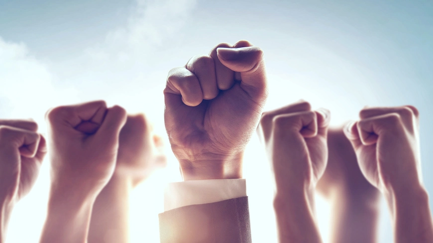 空に向かって拳を突き上げる複数の手が象徴する、団結・決意・行動の力強いイメージ